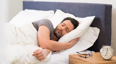 Handsome man sleeping in his bedroom. Man sleeping with alarm clock in foreground. Serene latin man sleeping peacefully.