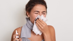 Image of ill allergic woman blowing running nose, having got flu or catch cold, sneezing in handkerchief, posing with closed eyes isolated on white studio background, holding nasal spray in hand.