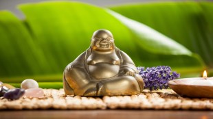 Laughing buddha figurine, lit candle and pebbles stone