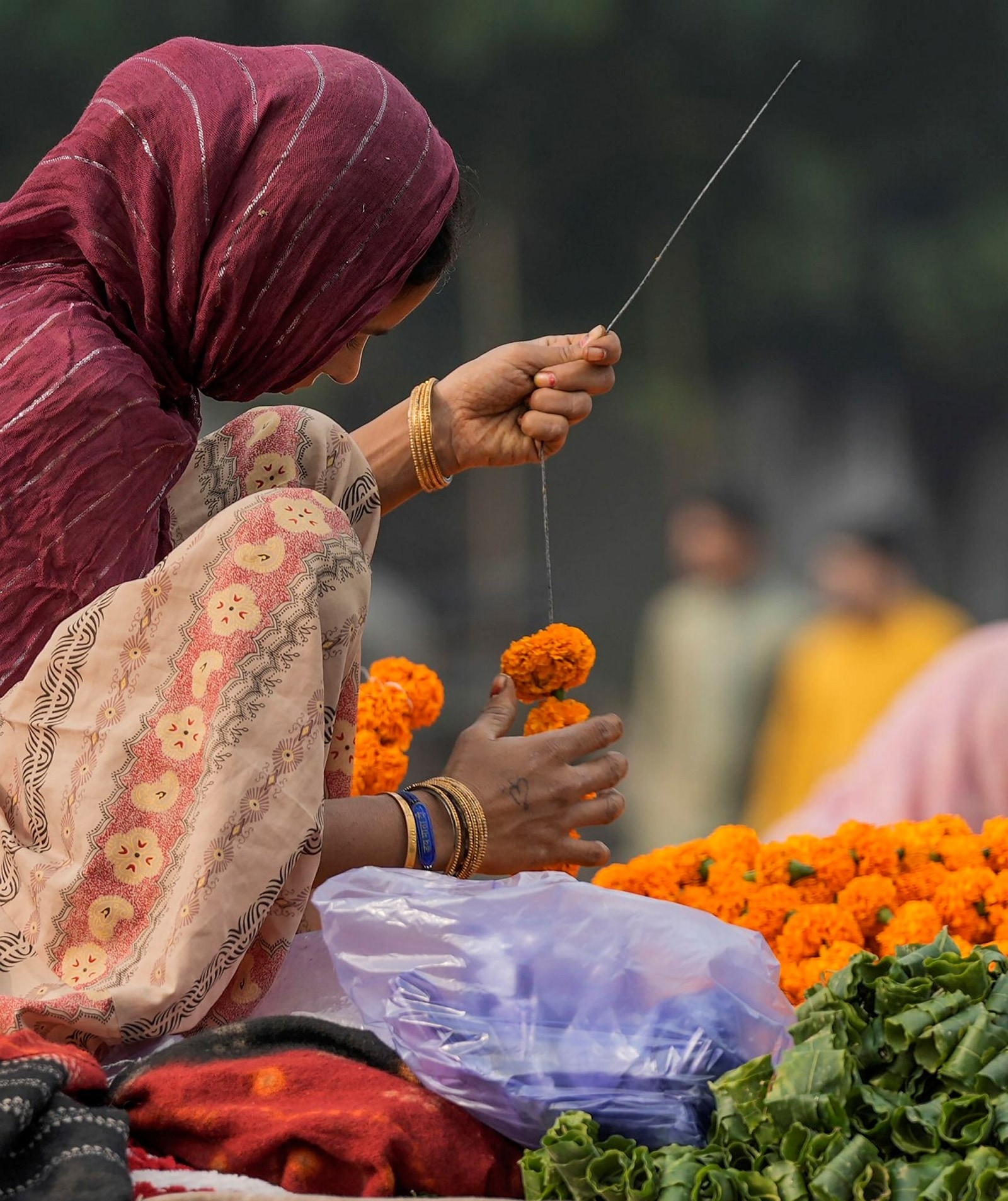 Gautam Buddha Nagar: A vendor makes garlands at her stall on a footpath during the festive season (PTI Photo/Vijay Verma)