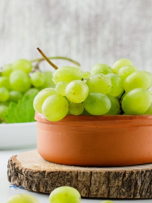 Grape clusters with wooden piece in plates on white and grungy background, side view.